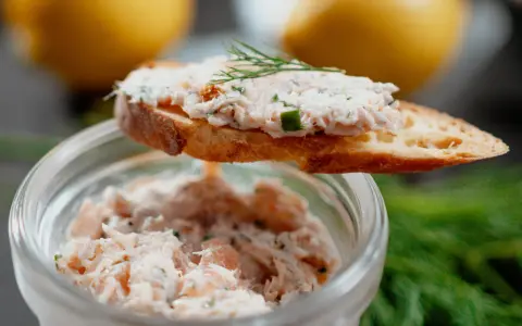 Un toast garni de rillettes de saumon, décoré d'aneth, avec un pot de rillettes en arrière-plan.
