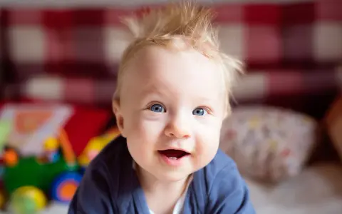 Uśmiechnięty niemowlak z niebieskimi oczami i wytartymi włosami na głowie, bawiący się zabawkami.