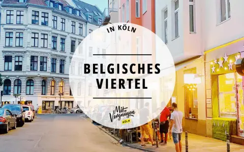 Abendstimmung im Belgischen Viertel in Köln. Menschen sitzen vor beleuchteten Geschäften, Autos parken am Straßenrand.