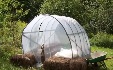 Un invernadero listo para el huerto de verano, con fardos de paja y carretilla a los lados.