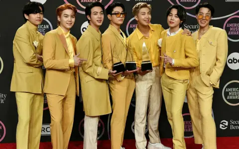 Medlemmar av BTS poserar glatt på röda mattan, klädda i matchande gula outfits och håller sina American Music Awards-troféer.