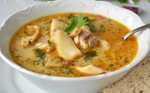 Sopa de pescado casera en un cuenco blanco con trozos de pescado, perejil y una rebanada de pan.
