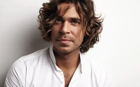 Hombre con cabello castaño ondulado, un ejemplo de cortes de pelo hombre medio largo, viste camisa blanca.