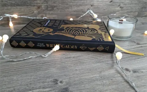 Książka "Wielki Gatsby" F. Scotta Fitzgeralda, otoczona świątecznymi lampkami, zaprasza do odkrycia jej streszczenia i historii.