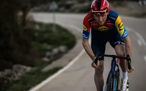 Tao Geoghegan Hart im roten Trikot auf einer kurvigen Straße, konzentriert auf das Rennen.