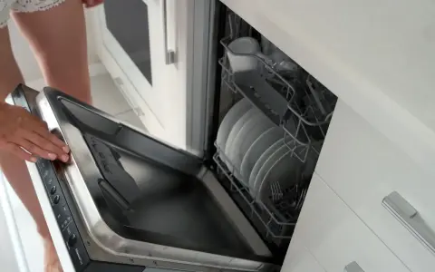 Montaż frontu do zmywarki Whirlpool. Kobieta otwiera drzwi zmywarki z załadunkiem naczyń.