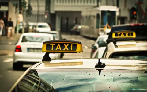 Ein Taxi mit leuchtendem "TAXI"-Schild auf dem Dach, bereit für Fahrten, auch im nachttarif. Regentropfen auf der Windschutzscheibe.