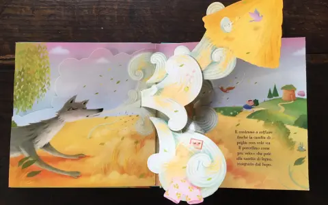 Libri pop-up più belli: un lupo soffia su una casetta di paglia, mentre un maialino corre verso una casetta di legno.