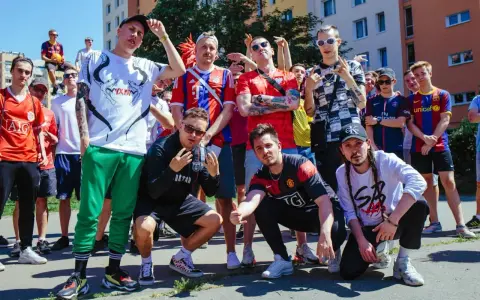 Grupa młodych ludzi w strojach piłkarskich, pozująca do zdjęcia. W tle budynki mieszkalne. To świetny **reto tekst** dla fanów futbolu.