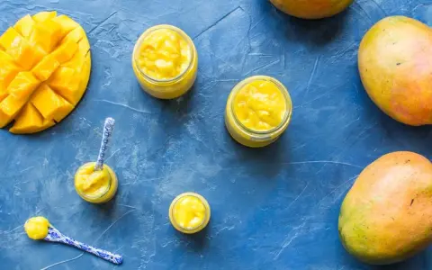 Délicieux curd mangue dans des petits pots, avec des mangues fraîches et des cuillères décorées. Un délice tropical !