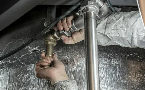 Instalator dokręca złączkę, by zapobiec dostawaniu się powietrza w rurach od wody.