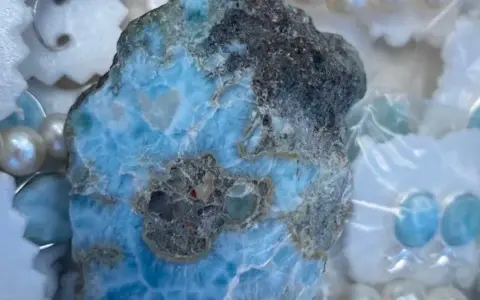Surowy larimar, kamień o niebiesko-białych żyłkach, otoczony perłami i ozdobami. Jego magiczne właściwości uspokajają i przynoszą harmonię.