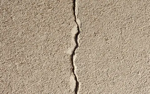 Grosse fissure sur un mur extérieur en crépi. Il faut réparer cette fissure pour éviter qu'elle ne s'aggrave.