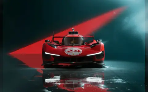 Czerwony samochód wyścigowy Ferrari 499P z numerem 24 na tle czerwonego światła.