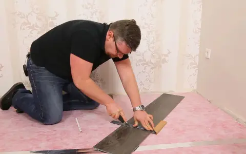 Mann kniet und schneidet mit einem Cuttermesser und Lineal eine Diele für den vinylboden verlegen.