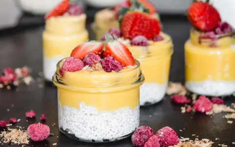Erfrischender Mango Chia Pudding in Gläsern, garniert mit Erdbeeren und Himbeeren. Ein gesunder Genuss!