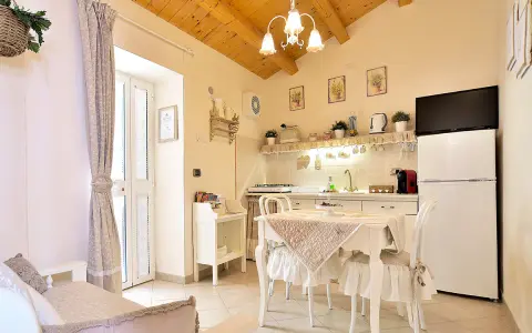 Cuisine et coin repas dans un style shabby chic, avec des meubles blancs, des textiles doux et des poutres apparentes.