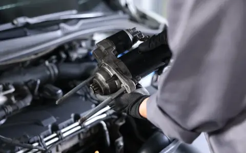 Mechanik w rękawiczkach trzyma rozrusznik na krótko, gotowy do montażu w silniku samochodu.