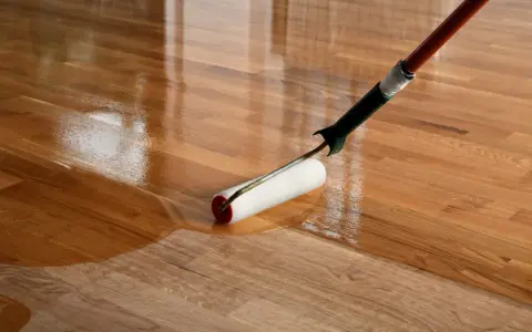 Application d'un vernis ou vitrificateur sur un parquet en bois. Le rouleau dépose une couche brillante et protectrice.