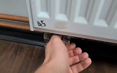 Ręka reguluje zawór grzejnika aluminiowego, próbując wyeliminować szum w grzejnikach aluminiowych.