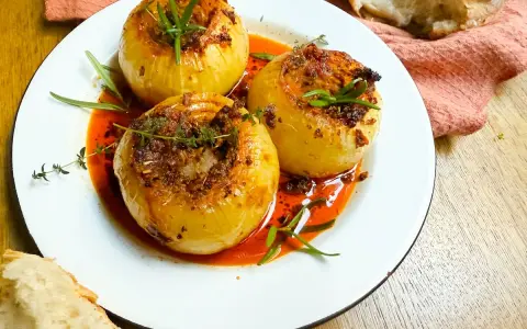 Tres cebollas al horno, rellenas y doradas, nadan en una salsa roja vibrante. Hierbas frescas coronan cada una.