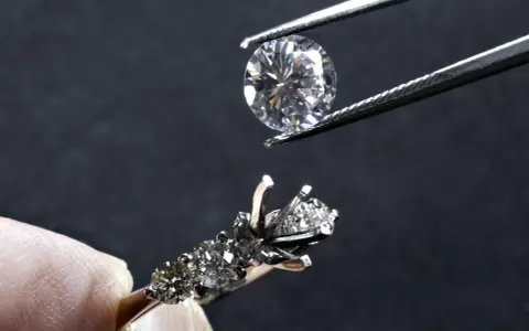 Un diamante viene posizionato con una pinzetta su un anello con incastonatura a castone ribattuto, pronto per essere fissato.