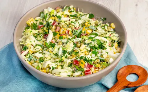 Schüssel mit knackigem Salat aus Weißkohl, Mais, Erbsen und Paprika, perfekt als salate zum vorbereiten am vortag. Mit frischer Petersilie garniert.