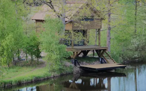 Drewniane domki wędkarskie nad jeziorem, otoczone zielenią, z pomostami schodzącymi do wody.