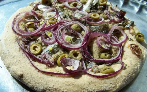 Pizza z anszua, oliwkami i czerwoną cebulą, gotowa do pieczenia.