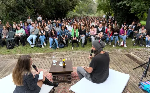 Un pubblico attento ascolta un dibattito all'aperto. Le parole fluiscono, profonde come il mare, leggere come il cielo.