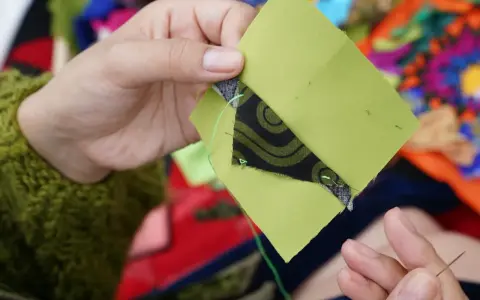Ręce szyją zielone kwadraty z czarnym wzorem, tworząc patchwork projekty.