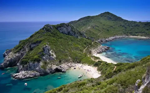 Malownicza zatoka z turkusową wodą i piaszczystą plażą, otoczona zielonymi wzgórzami. Tak właśnie wygląda Korfu, grecka wyspa, gdzie leży ten raj.