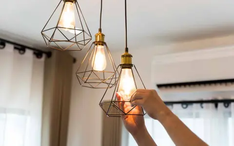 Man changing a lightbulb in a modern geometric pendant lamp, part of the simple home interiors.