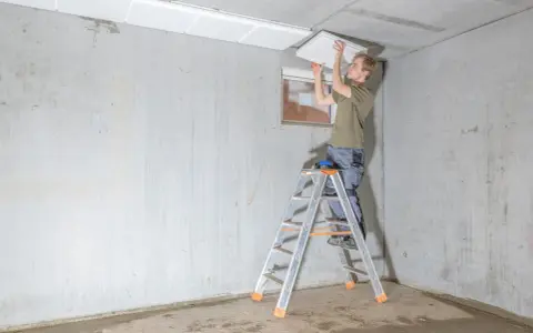 Mann auf Leiter montiert weiße Platten zur kellerdecke isolieren.