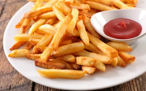 Une assiette de frites au four dorées et croustillantes, accompagnées d'un petit bol de ketchup rouge vif.