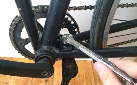 Montaż stopki rowerowej. Klucz dokręca śrubę mocującą stopkę do ramy roweru, obok korby i łańcucha.