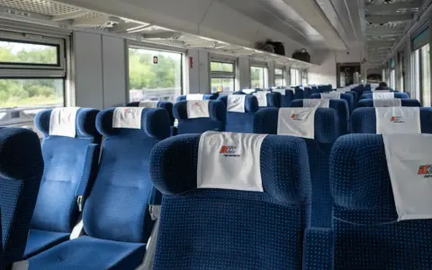 Puste niebieskie siedzenia w wagonie PKP Intercity z zagłówkami z logo.