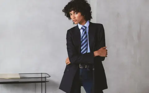 Persona androgina con traje a rayas, camisa azul y corbata a juego, posando con confianza.