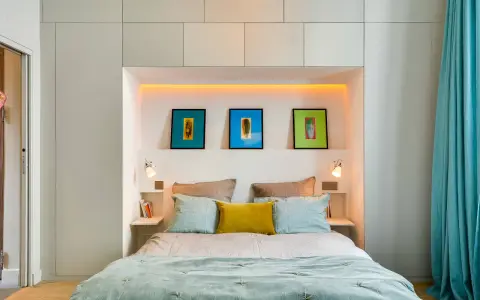 Idee salvaspazio camera da letto piccola: letto con testiera contenitore, quadri colorati e tende turchesi creano un ambiente accogliente.