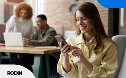 Uśmiechnięta kobieta korzysta z telefonu, podczas gdy koledzy pracują przy laptopie. To obraz skutecznego digital branding.