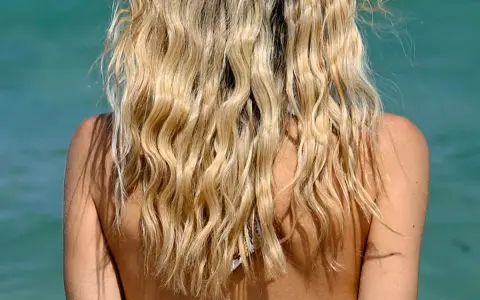 Blondes Haar mit Beach Waves im Meer. Die Sonne scheint auf die Schultern.