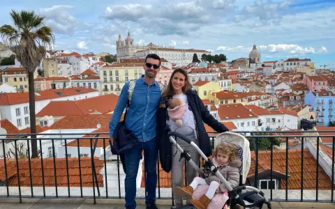 Familia disfrutando de las vistas de Lisboa con niños. Un bebé en portabebés y una niña en carrito, con la ciudad de tejados naranjas de fondo.