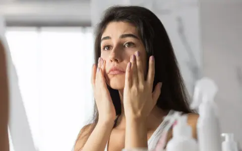 Donna preoccupata si tocca il viso, notando i segni dello stress sulla pelle.