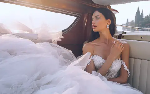 Sposa con abito bianco e trucco impeccabile, seduta su una barca, con il velo che ondeggia al vento.