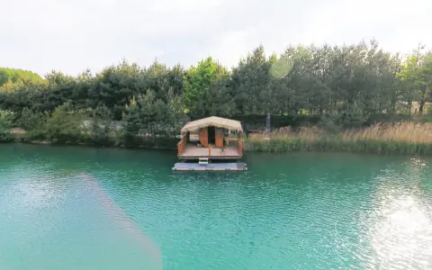 Drewniana chata na wodzie, otoczona lasem, unosi się na turkusowym zalewie.
