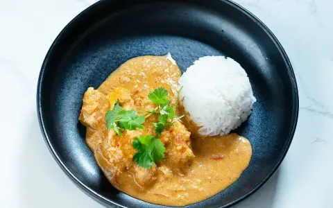 En krämig butter chicken med ris och färsk koriander i en svart skål.