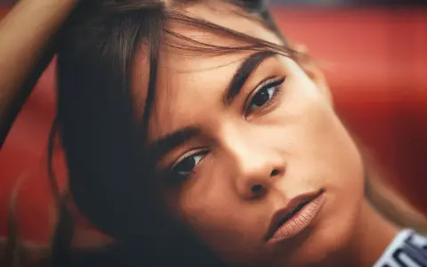 Portrait d'une jeune femme aux gros sourcils, la main dans les cheveux, regard intense.