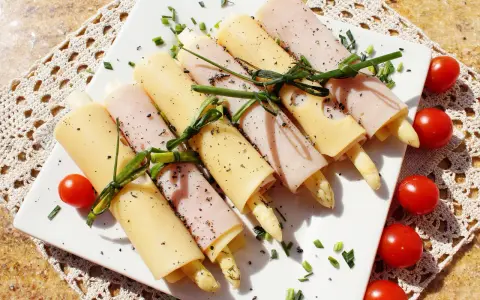 Roladki ze szparagami, zawinięte w szynkę i ser, ozdobione szczypiorkiem i pomidorkami. Pyszna przekąska.