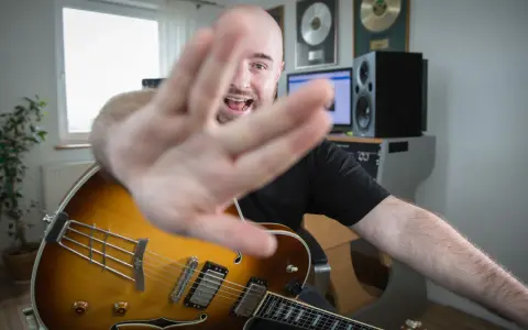 Muzyk z gitarą jazzową, z ręką na pierwszym planie, śpiewa, wyjaśniając, akord co to.