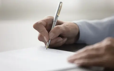 Dłoń pisze długopisem na dokumencie. To ważny moment, jak napisać testament, by wszystko było jasne.